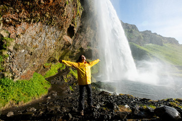 Happy tourist under Seljalandfoss waterfall, Iceland (water splashes all around) - obrazy, fototapety, plakaty