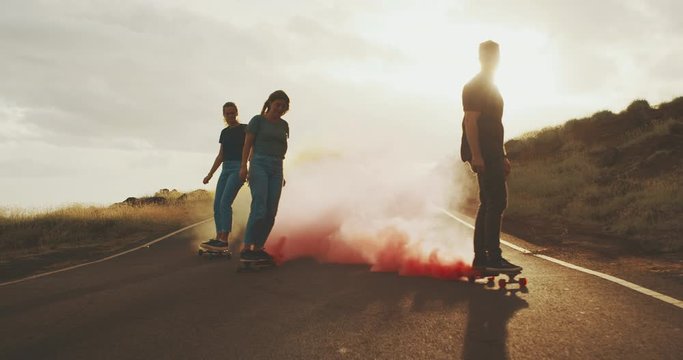 Three adventurous friends skateboarding with colorful pink smoke trails at sunset, skateboarding with smoke grenades at sunset