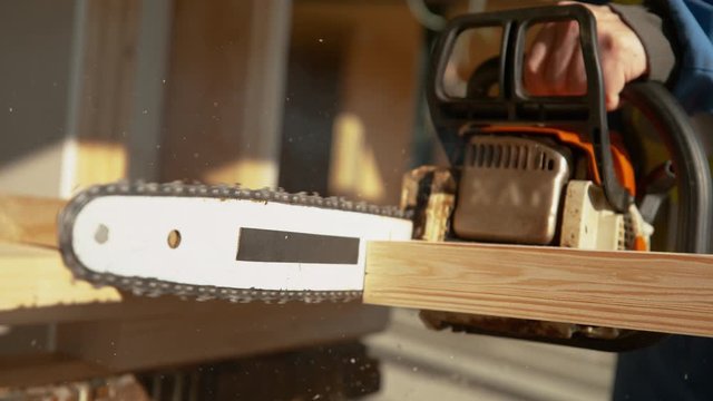 SUPER SLOW MOTION, CLOSE UP, DOF: Experienced builder cuts a beam in two pieces with a large chainsaw while building a house. Unrecognizable worker uses a chainsaw to cut a plank into two pieces.