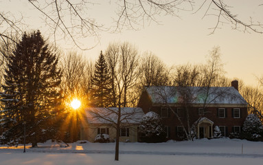 winter scene with sun setting behind home  in New England