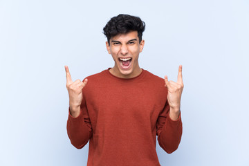 Young Argentinian man over isolated blue background making rock gesture