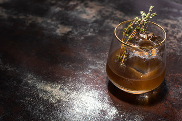 transparent glass with herb, ice cube and whiskey on weathered surface
