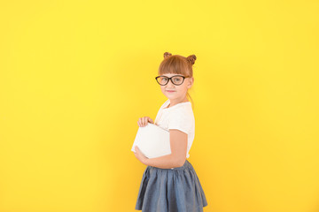 Cute little girl with book on color background
