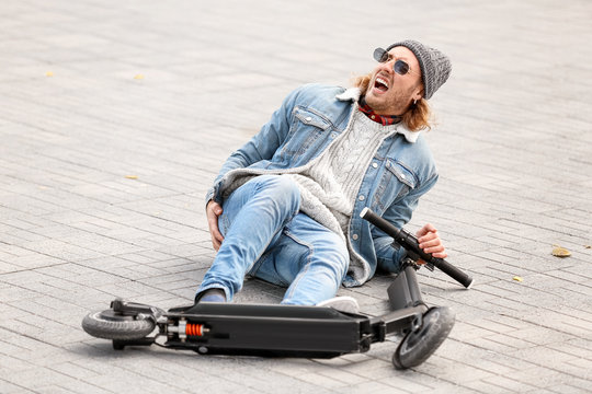 Young man fallen off his kick scooter outdoors