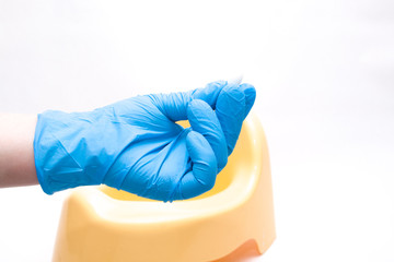 a hand in a disposable blue medical glove holds an anal suppository, in the background is a yellow children’s pot, white background, copy space