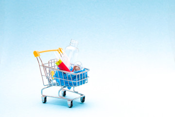 disposable plastic white plug, battery, plastic bag, light bulb and bottle in a shopping trolley on a blue background copy space, zero waste lifestyle concept.