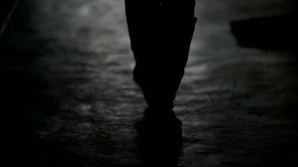 Dark exposure silhouette of a woman view from the back in defocus. A female figure is walking along a dark corridor, moving away from the camera.