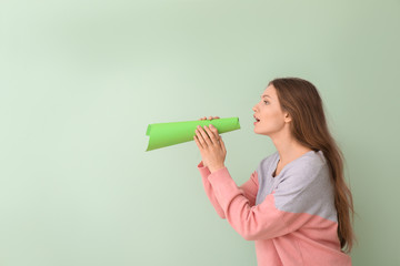 Young woman with paper megaphone on color background