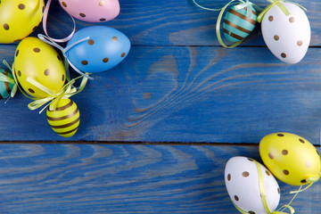 Easter background. Flat lay. Background of bright Easter eggs of different colors on a blue wooden background. Painted eggs. Close-up, horizontal, cropped shot, free space in the center of the frame. 