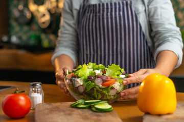 Female chef presenting a glass bowl of freshly made healthy vegetable salad in a rustic type kitchen. 