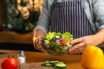 Female chef placing a glass bowl of freshly made healthy vegetable salad on a kitchen counter in a rustic type kitchen