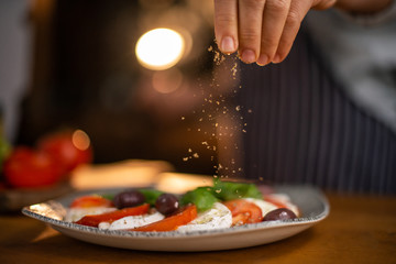 Close up of female chef hands seasoning a plate of freshly made tomato and mozzarela salad. 