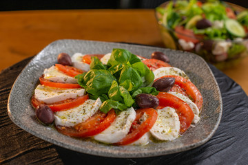 Close up of a plate of delicious and fresh tomato and mozzarella salad, placed on a wooden cutting board in a restaurant or a kitchen.