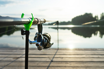 Carp fishing on beautiful blue lake with carp rods and rod pods in the summer morning. Fishing from the wooden platform.