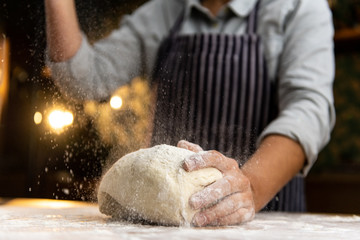 Female chef is kneading dough on a wooden surface, sprinkling it with flour