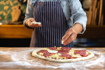 Obraz na płótnie Canvas Female chef is placing slices of fresh mozzarella cheese on traditional, homemade pizza.