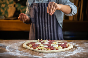 Female chef is sprinkling fresh oregano over a traditionally made home pizza. 
