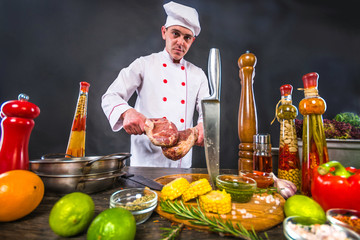 Catering business. Chef in white uniform planning to cook a beef tomahawk steak. Appetizing cooking background.