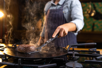 Female chef is grilling juicy, delicious, meat burgers on a kitchen stove in a restaurant.