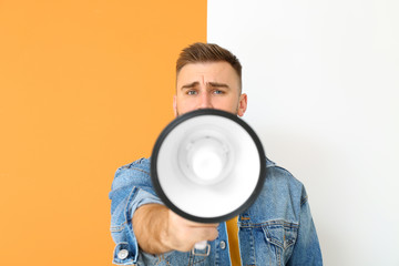 Emotional young man with megaphone on color background