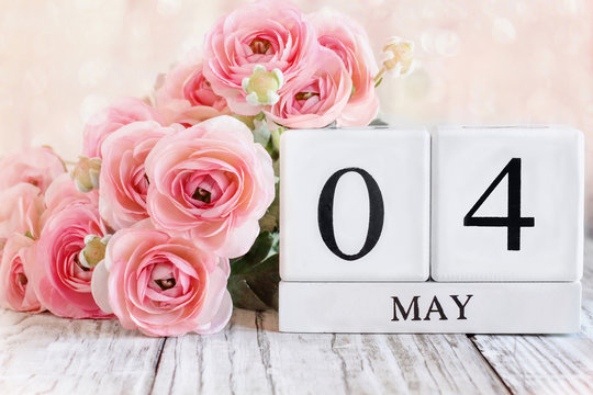 White wood calendar blocks with the date March 18th and pink ranunculus flowers over a wooden table. Selective focus with blurred background.