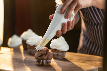 Close up of a chef pouring whipped cream over a freshly baked cupcake