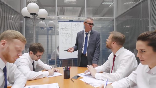 Senior executive leader coach talks at business meeting makes presentation for corporate workers, colleagues group. Employees listen to mature speaker. Training of professional team at seminar