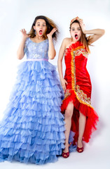 Fototapeta na wymiar Two excited pretty young festively dressed girls wearing makeup standing isolated over light background. Wow concept. Isolate glamorous and beautiful girls in bright clothes, having fun. Isolate