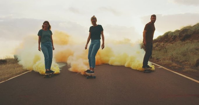 Three stylish carefree friends skateboarding at sunset with colorful smoke trails, fun skateboarding with smoke grenades