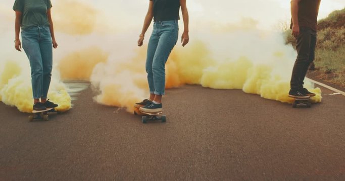Three stylish carefree friends skateboarding at sunset with colorful smoke trails, fun skateboarding with smoke grenades