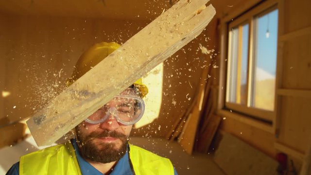 SLOW MOTION, CLOSE UP, PORTRAIT: Wooden board falls on a worker's head. Small plank falls from above on an unsuspecting contractor's head. Yellow hard hat saves Caucasian builder's from a concussion.