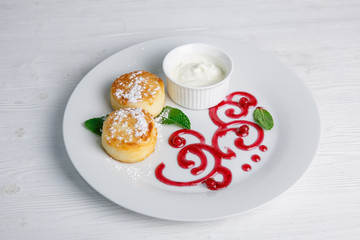 Cottage cheese pancakes or cheesecakes with sour cream on a white ceramic plate are decorated with jam. Delicious Breakfast or brunch. Menu