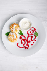 Cottage cheese pancakes or cheesecakes with sour cream on a white ceramic plate are decorated with jam. Delicious Breakfast or brunch. Menu