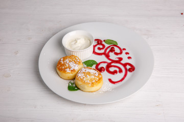 Cottage cheese pancakes or cheesecakes with sour cream on a white ceramic plate are decorated with jam. Delicious Breakfast or brunch. Menu