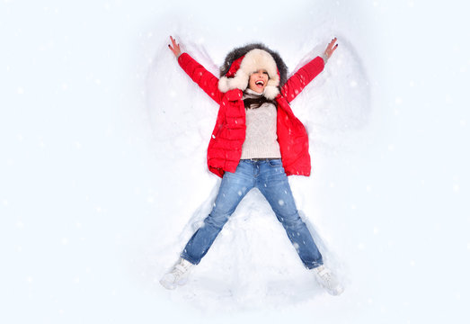 Snow angel concept. Happy woman enjoying first snow, lying in snow and making snow angel. Winter holidays and entertainment background.