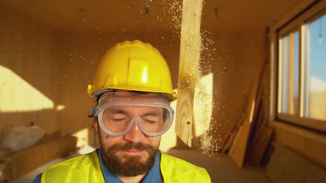 SLOW MOTION, CLOSE UP, PORTRAIT, DOF: Experienced builder is struck from above by a falling wooden beam. Yellow safety helmet saves Caucasian worker's from a bad concussion. Construction site hazard.