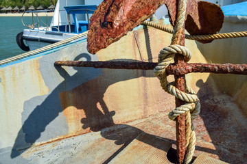 Thick rope wound on rusty anchor in a boat in sea in tropics