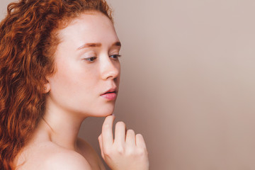 very beautiful girl with red curly hair without makeup looks away on a beige background in the studio. Natural beauty concept