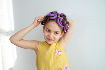 a little girl pretends to be an adult woman or her mommy with curlers in her hair. The concept of kids pretending to be adults.