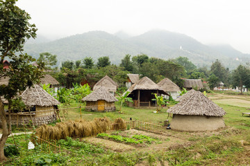 Fototapeta na wymiar View on wooden houses and garden on a background of mountains in cloudy weather. Pai, Mae Hong Soon Province, Thailand.