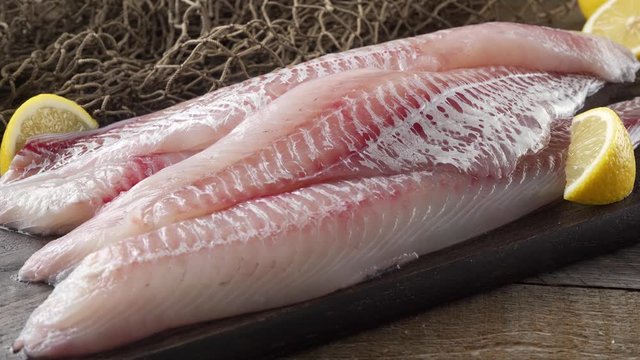 Fresh haddock fillets on a cutting board with lemon wedges.