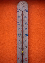 A huge wooden thermomater showing minus degrees, in front of a bright orange wall.