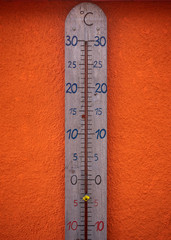 A huge wooden thermomater showing minus degrees, in front of a bright orange wall.