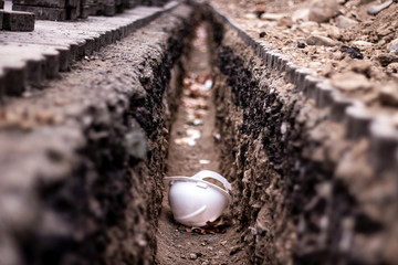 Underground road communications working. Protective helmet in earthen trench. Road rehabilitation. 