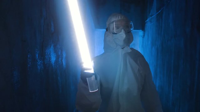 Hazmat suit wearing woman explores a dark tunnel. Female in protective suit, mask and glasses with flashlight walking in dark tunnel, looks around.