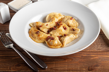 Dumplings and ravioli stuffed with meat. Sprinkle sliced smoked tomatoes. Served on a large white plate. Next to a bowl of sour cream. On a wooden background.