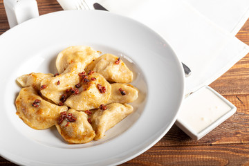 Dumplings and ravioli stuffed with meat. Sprinkle sliced smoked tomatoes. Served on a large white plate. Next to a bowl of sour cream. On a wooden background.