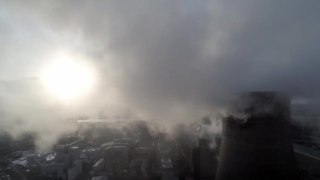 Aerial pull back reveal of UK power station cooling towers through atmospheric steam emissions at sunrise.