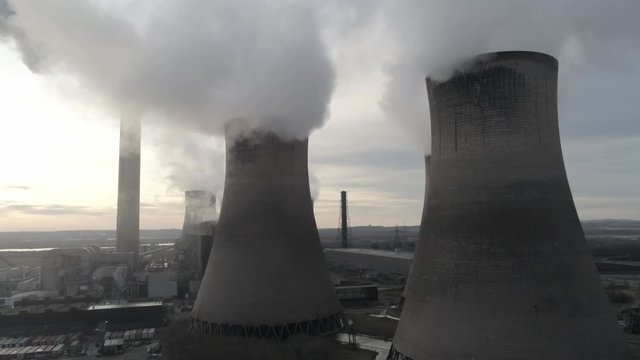 Aerial view rising to UK power station cooling towers atmospheric smoke steam emissions at sunrise.