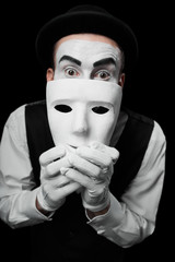 Mime artist hiding under white mask. Isolated on black background. Concept of people masks and lies